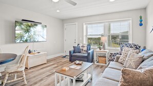 A spacious living room with a ceiling fan, a flat-screen TV, a dining table, and a comfortable seating area with a couch and chairs. - Stay in this 3BR/2BA condo you may never want to leave! (Port Aransas)