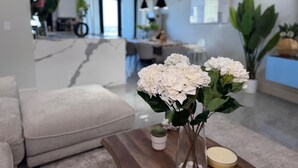 Ein modernes Wohnzimmer mit Marmorwand, einem weißen Sofa und einer Vase mit weißen Blumen auf einem Holztisch.