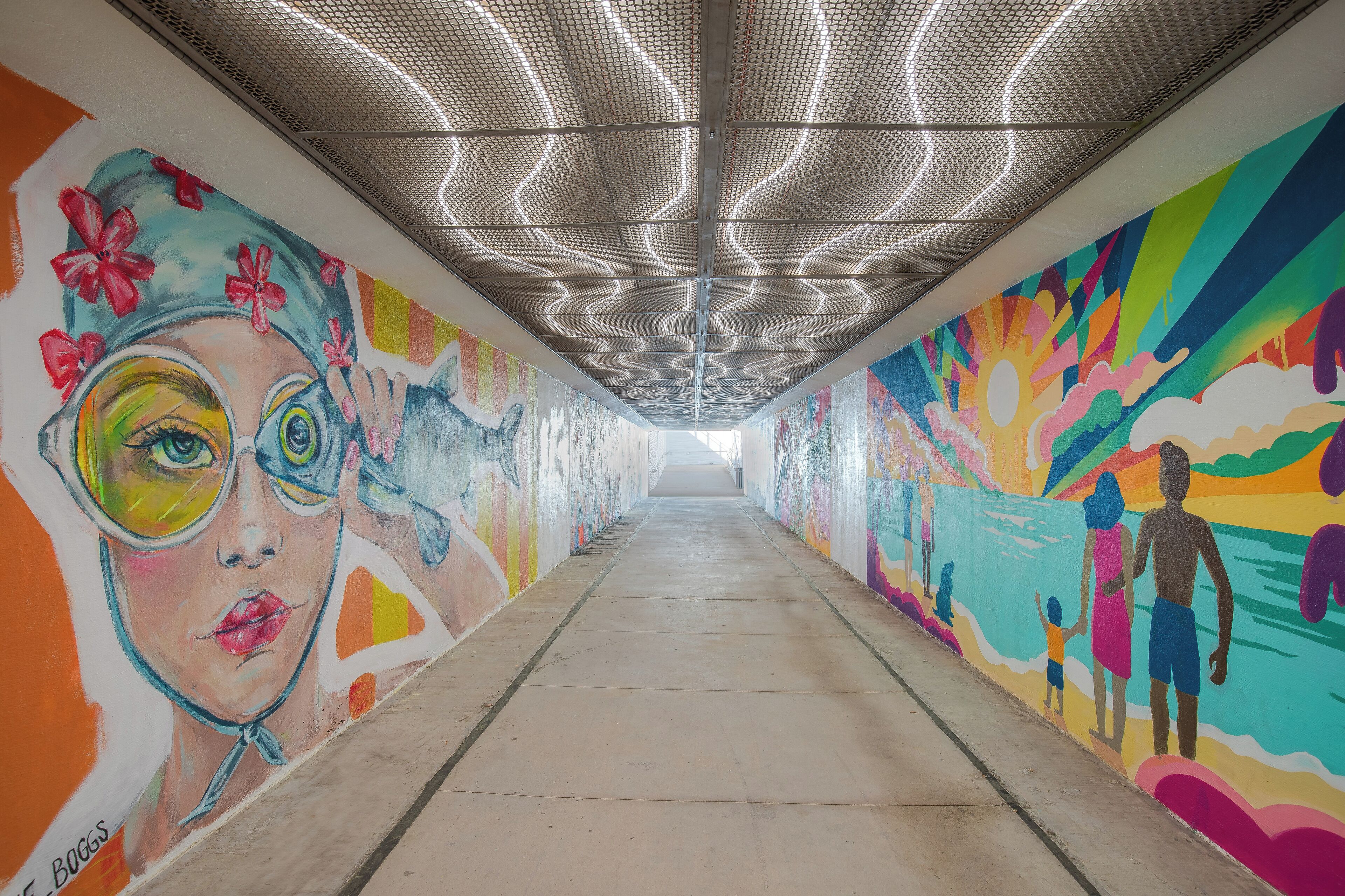 A brightly colored corridor with murals on the walls, a patterned ceiling, and a concrete floor.