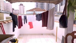 Un balcon avec du linge séchant sur un fil à linge, une chaise, une table et un panier jaune.