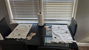 Ein Essbereich mit Tisch für zwei Personen, ausgestattet mit einer weißen Tischdecke mit Bienenstickerei, einer gewebten Tischunterlage und einem Kerzenhalter.
