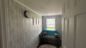 Un pasillo con pared de madera, un tapete redondo, un sofá gris y una ventana con persianas.