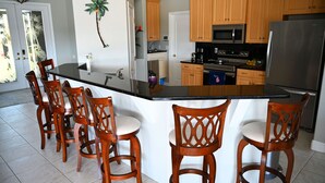 Una cocina con armarios de madera, encimera negra y refrigerador de acero inoxidable.