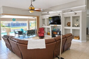 A living room with a brown leather sofa, a red chair, a television, and a ceiling fan. - Villa Pelican Point by swflorida-villas with gulf access  in SW Cape Coral (Cape Coral)