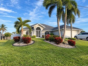 A residential house with a well-maintained lawn, palm trees, and a garage.