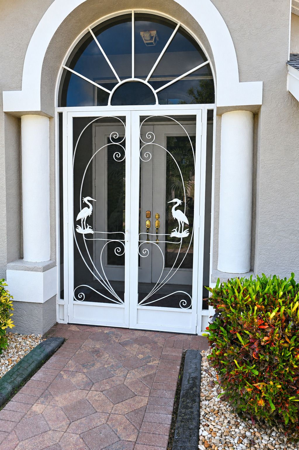 A building entrance with a double door featuring decorative metalwork and two white statues of birds.