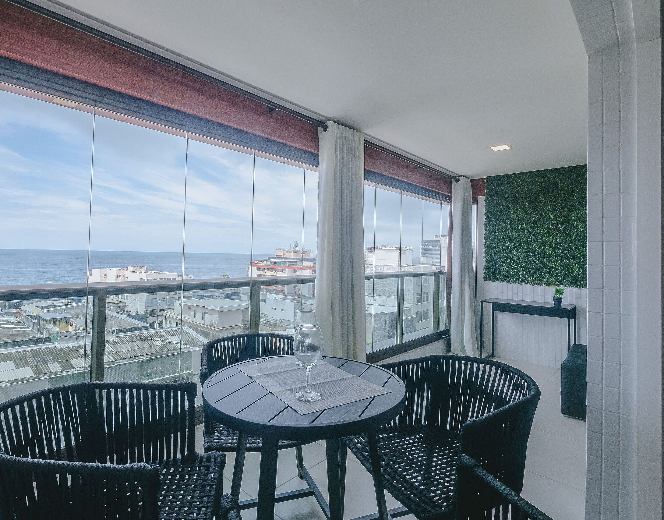 Un balcon avec une table et des chaises, une vue sur la mer et un mur végétal.
