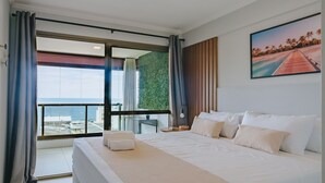 A hotel room with a large bed, a view of the sea, and a painting on the wall. - Dream stay just 250m from Praia do Farol (Salvador)