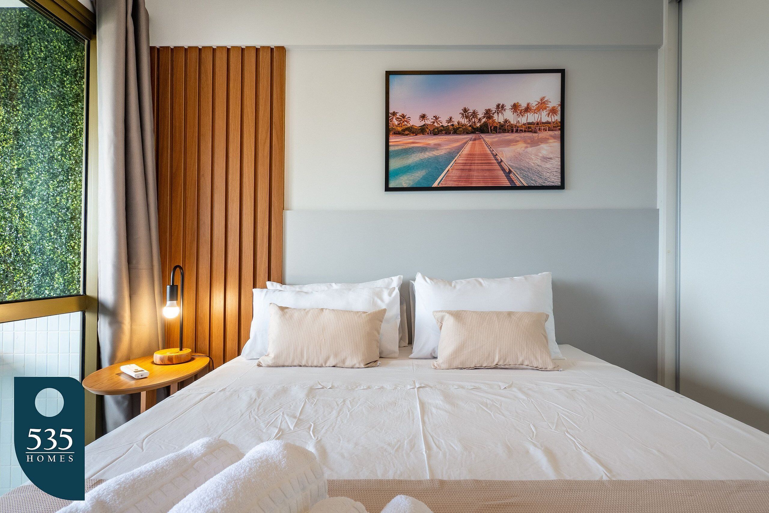 Une chambre d’hôtel avec un lit, une table de chevet, une lampe et un tableau représentant une scène de plage.