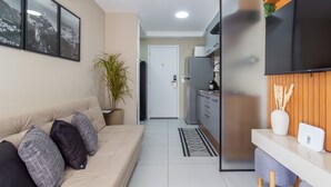 A modern living room with a sofa, a potted plant, and a kitchen area with a refrigerator and a flat-screen TV. - Close to Rio's city center | IM712 (Rio de Janeiro)