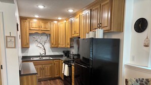 A compact kitchen with wooden cabinets, a black refrigerator, and a sink.