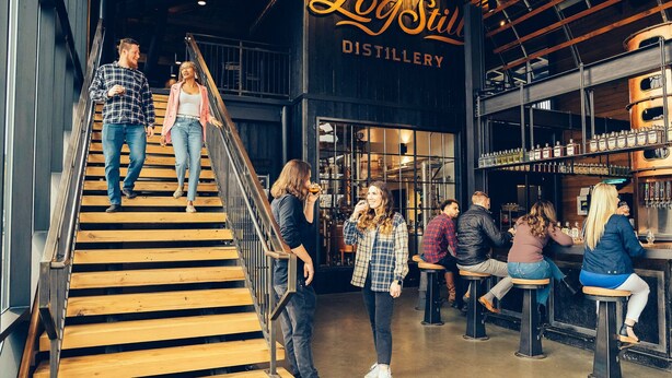 A distillery interior with wooden stairs, a bar area, and a sign reading "Leg Still Distillery".
