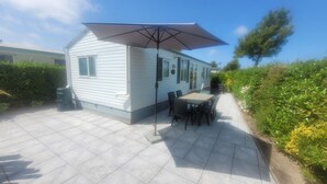 Una casa móvil con un patio amueblado, que incluye una mesa, sillas, una sombrilla y un pequeño jardín.