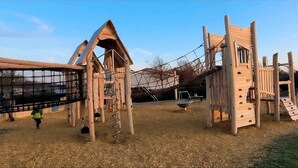 Un parque infantil con estructuras de madera para escalar y una red de cuerdas.