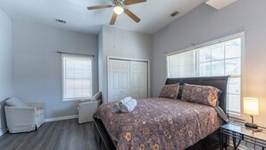 Um quarto com cama, ventilador de teto, janela e mesa de cabeceira.
