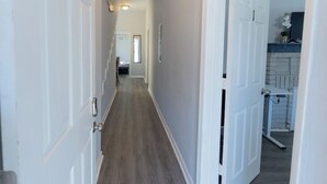 Um corredor com portas brancas, piso de madeira e vista para um quarto com lareira de tijolos.