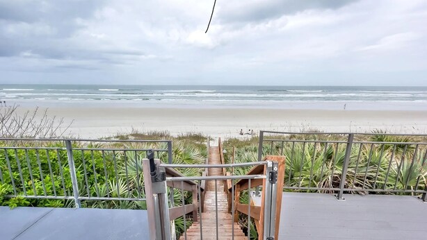 Una escalera de madera que lleva a una playa, con una barandilla de metal al frente.