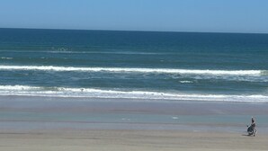Una playa con olas y una persona caminando.