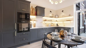 Una cocina moderna con muebles oscuros, horno empotrado y una zona de comedor para cuatro.
