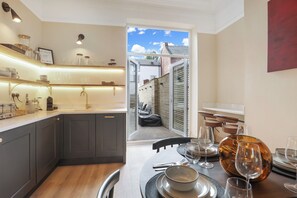 Una cocina moderna con armarios grises oscuros, una encimera de madera y un comedor con mesa dispuesta para cuatro personas. Un ventanal ofrece vistas al exterior.