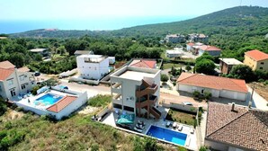 A residential area with houses, a swimming pool, and a hillside in the background.