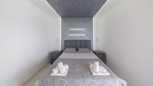 A modern hotel room with a large bed, two bedside tables, a grey headboard, and a grey ceiling.