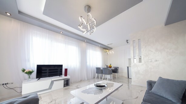 A modern living room with a flat-screen TV, a dining area with a table and chairs, and a gray sofa.