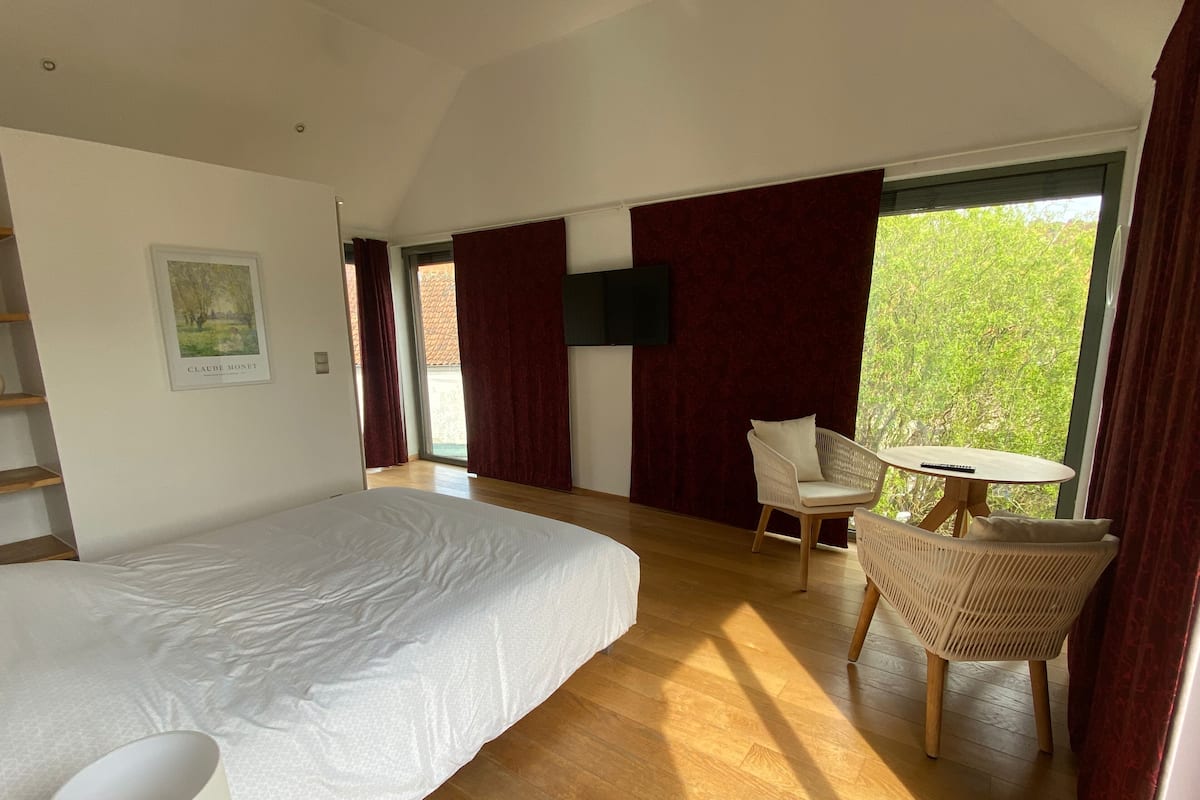 Ein modernes Schlafzimmer mit einem großen Bett, einem kleinen runden Tisch, einem Stuhl und einem an der Wand montierten Fernseher.
