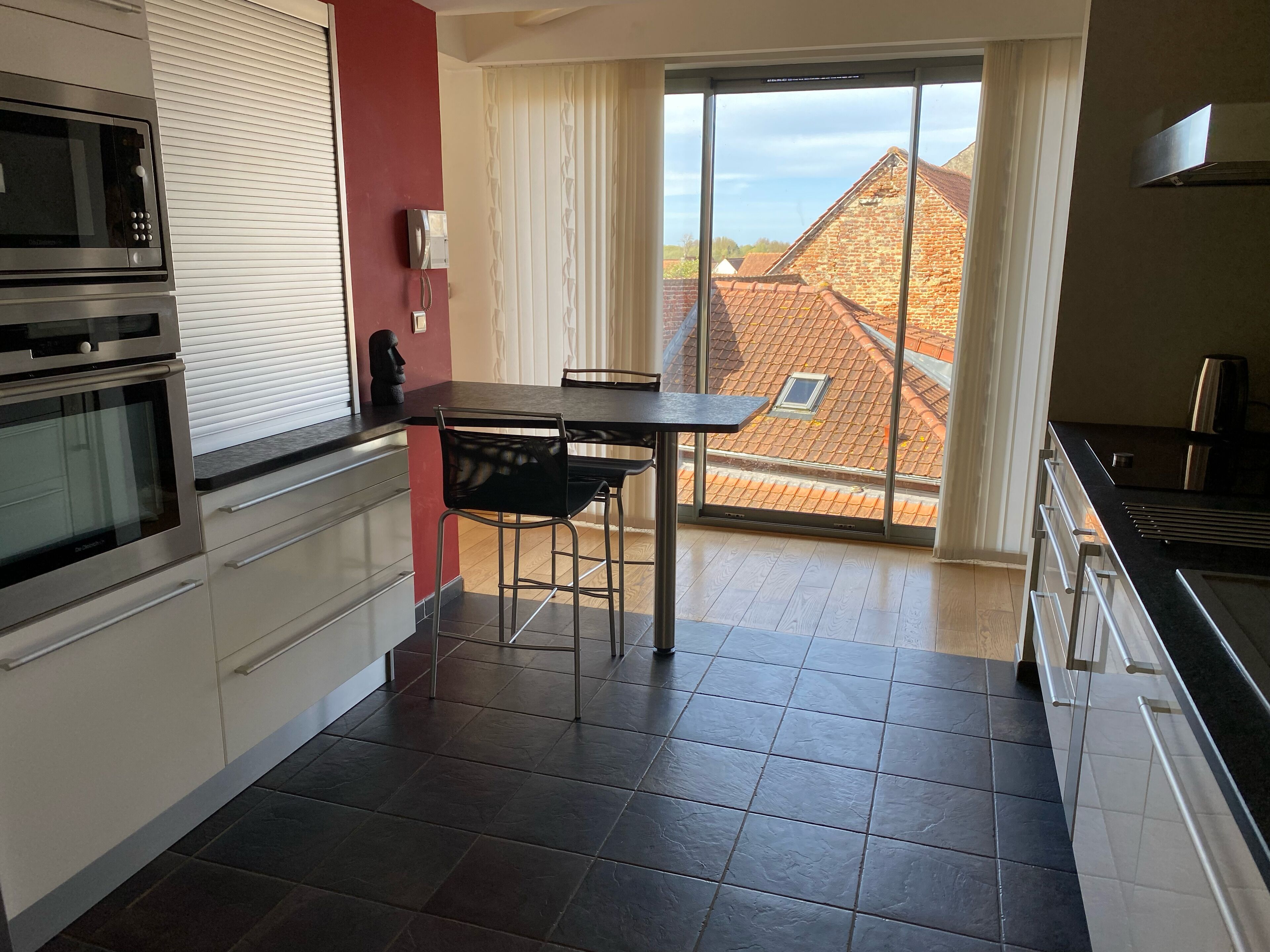 Una cocina moderna con comedor, ventanas amplias y vistas a edificios vecinos.