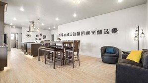 Ett modernt kök med träskåp, en matplats med bord och stolar samt ett vardagsrum med soffa och en lampa.