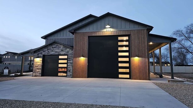 En modern byggnad med två stora garageportar, en fasad av sten och en täckt veranda.
