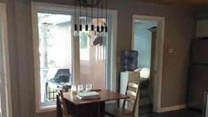 Un'area pranzo con tavolo e sedie in legno, una lampada a sospensione e vista all'esterno tramite una porta in vetro.