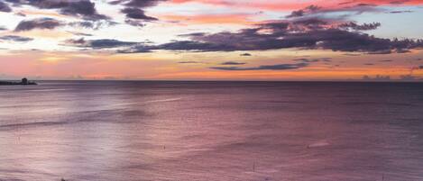 Una playa con un atardecer, palmeras y un barco a lo lejos.