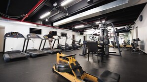 Une salle de sport équipée de tapis de course, d’un rameur et de divers appareils de musculation.