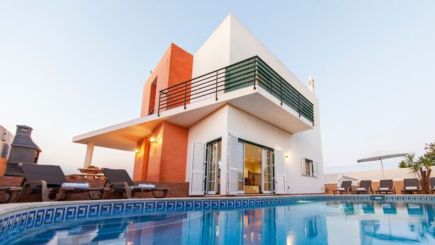 A modern two-story house with a swimming pool, featuring a balcony with a green railing. - Modern villa with BBQ and heatable pool (Albufeira)