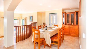 A dining area with a round table set for six, wooden chairs, and a kitchen with wooden cabinets. - Modern villa with BBQ and heatable pool (Albufeira)