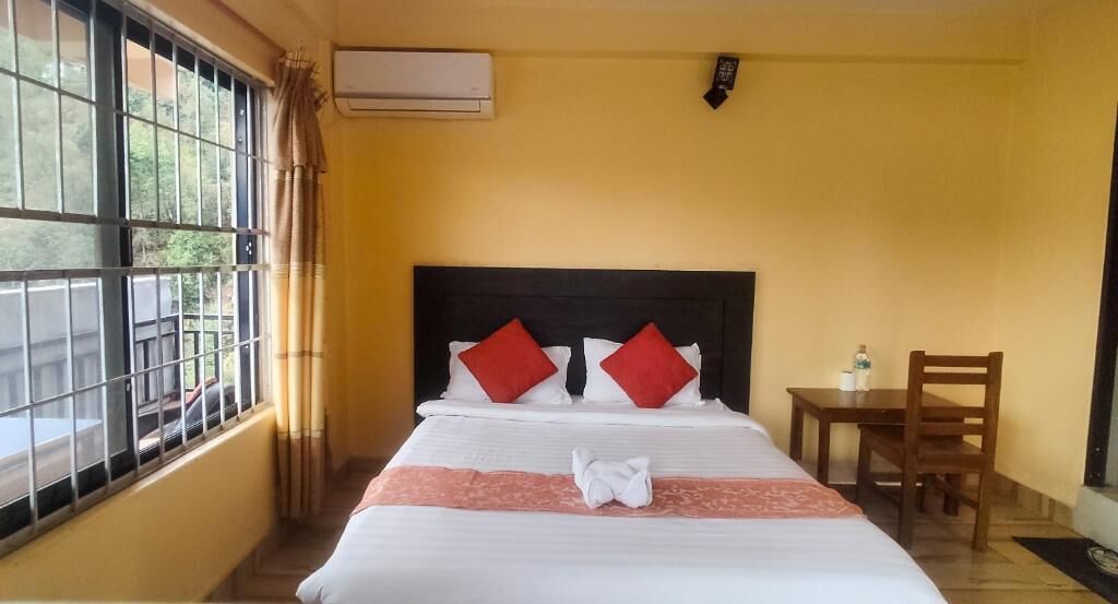 A hotel room with a bed, a window with bars, a bedside table, and a chair.