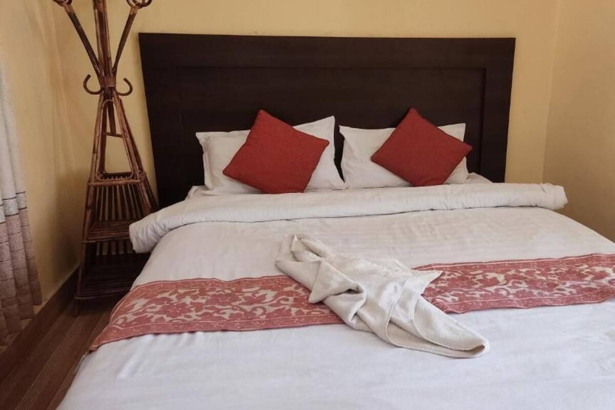A neatly made bed with white linens, red pillows, and a folded towel on the bed.