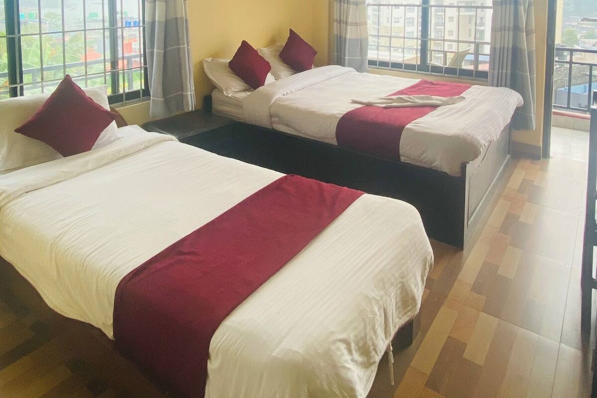 A hotel room with two beds, a ceiling fan, large windows, and a view of the city.
