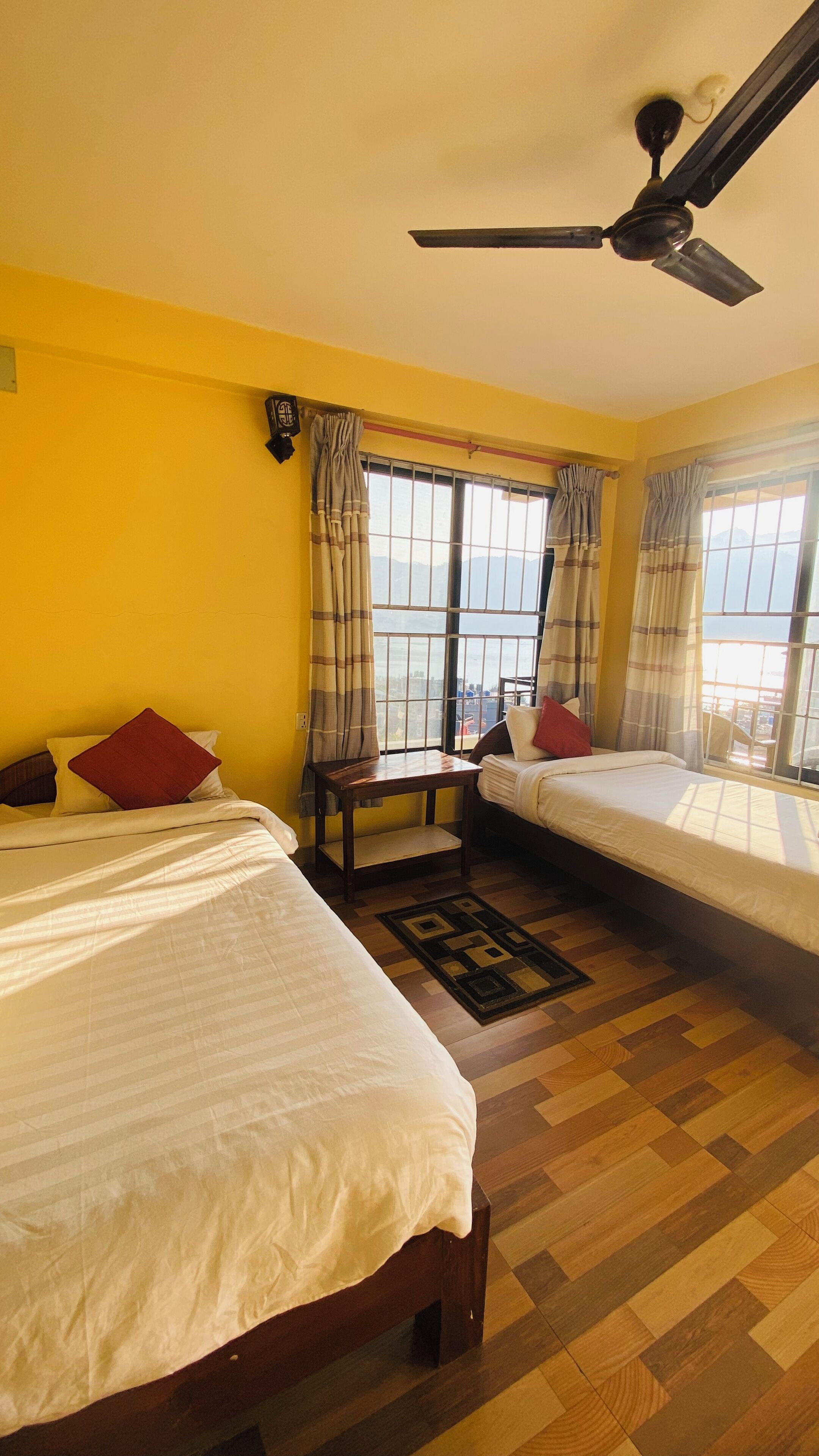 A hotel room with two beds, a ceiling fan, and large windows with curtains.