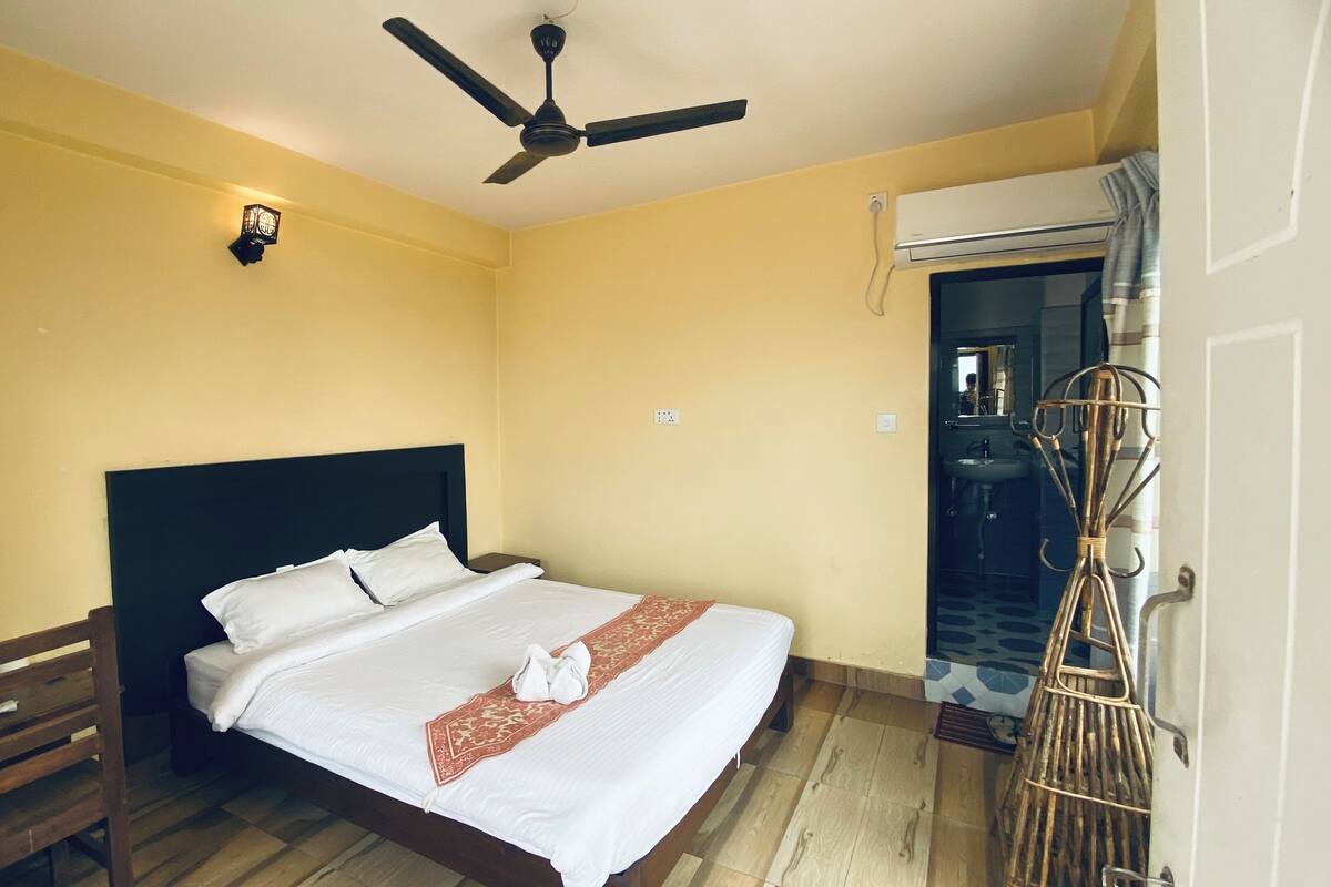 A hotel room with a bed, a nightstand, a ceiling fan, a wall-mounted light, and an air conditioning unit.