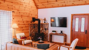 Ein gemütliches Wohnzimmer mit Kamin aus Stein, Holzwänden, einem Fernseher und bequemen Sitzmöglichkeiten.