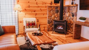 Ein gemütliches Wohnzimmer mit Kamin aus Stein, einer Couch, einem Holztisch und einer Lampe.