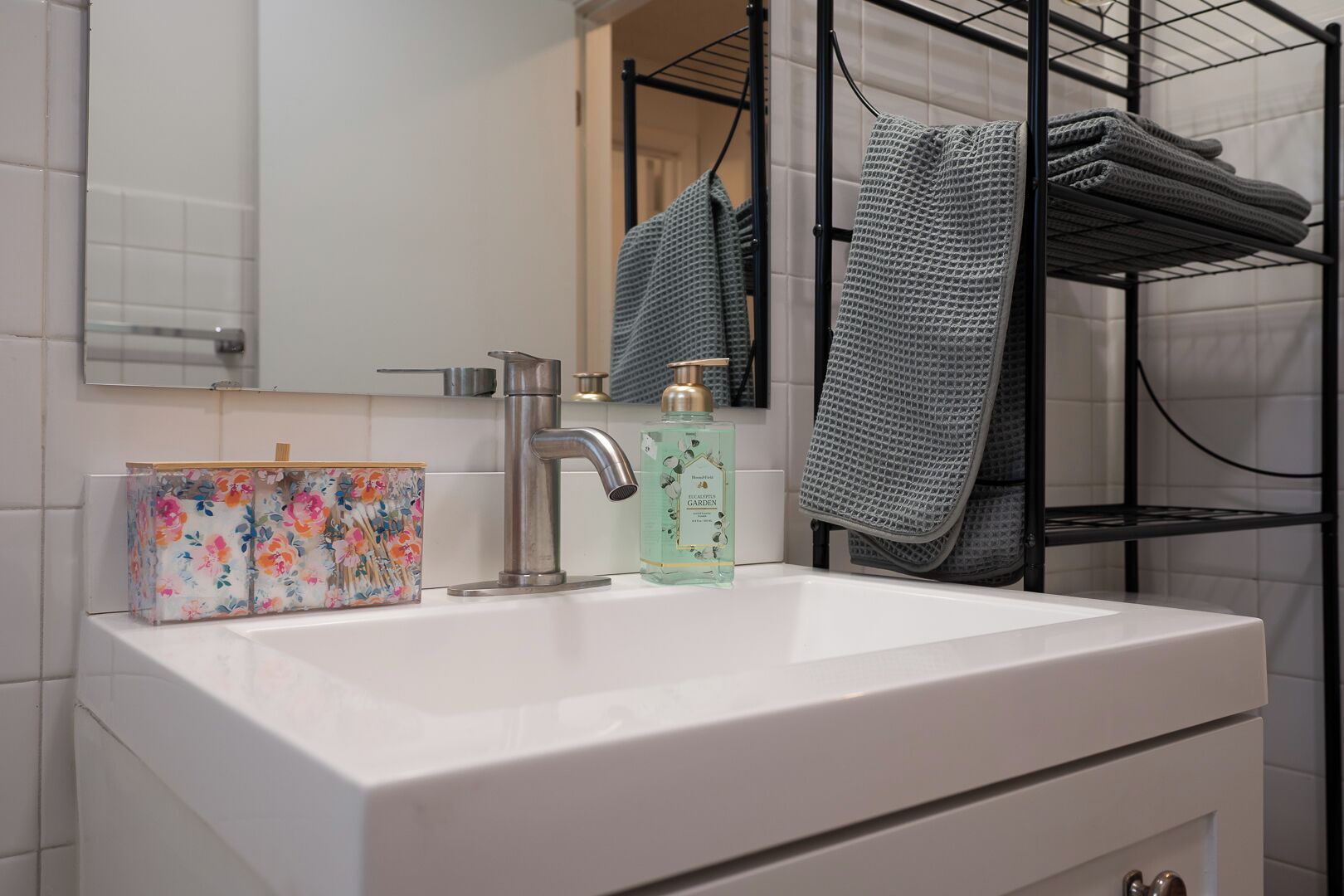Bany amb un lavabo blanc, un aixeta modern, una caixa de sabó floral i una ampolla de sabó de mans.