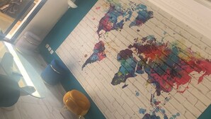 A room with a world map mural, a blue and white tiled floor, a red and gold ottoman, and a window with curtains. - Furnished and air-conditioned 2-bedroom apartment living room (Dakar)
