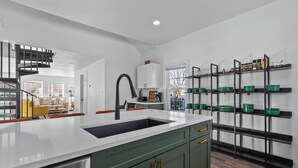 A modern kitchen with a central island, green cabinetry, and a built-in shelf unit with green bowls.