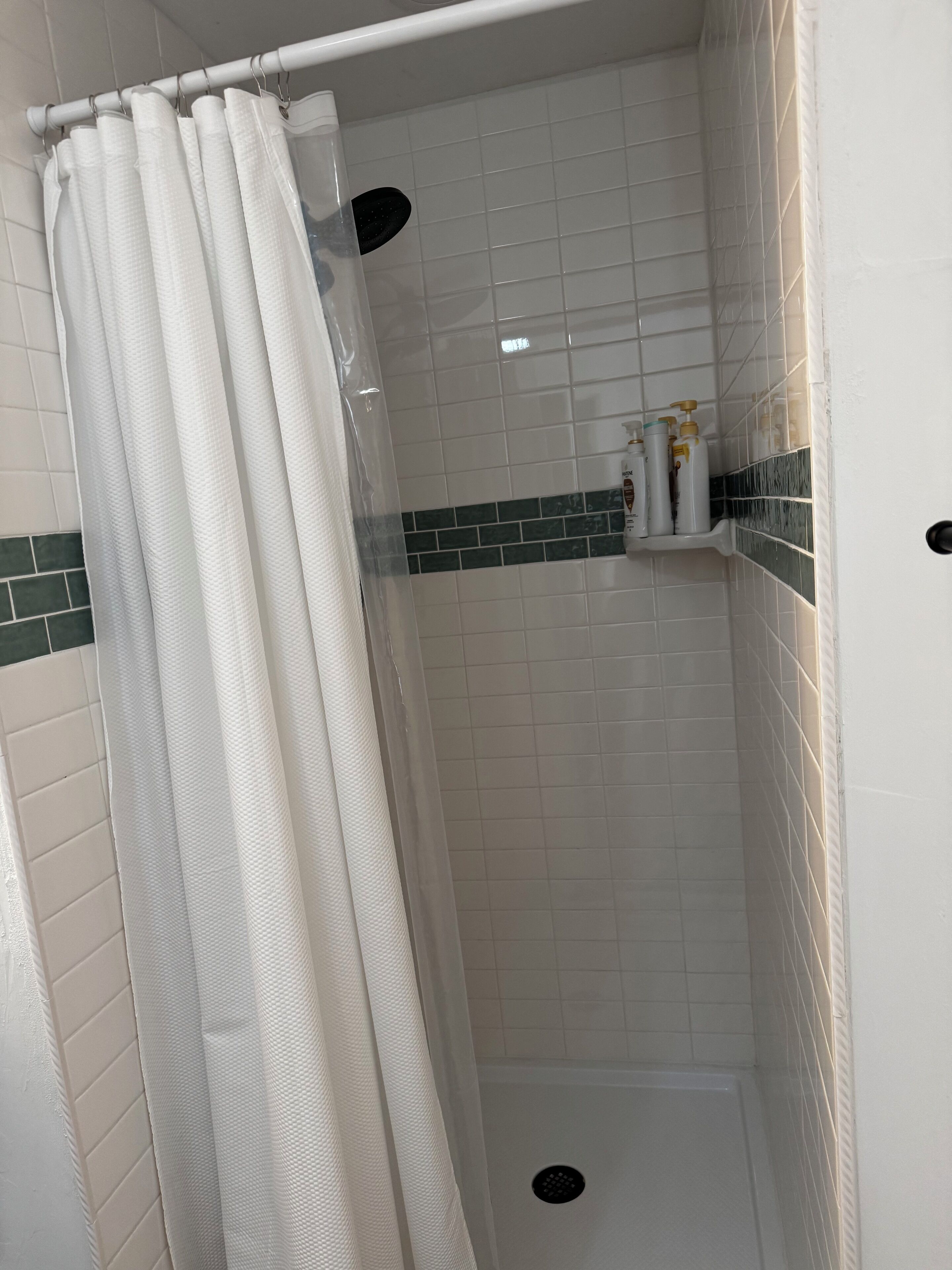 A shower area with white tiles, a shower curtain, and a shelf with toiletries.