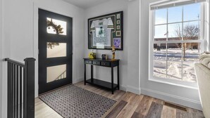 A modern entryway with a black door, a console table with memorabilia, a patterned rug, and a large window with a view of a snowy landscape.