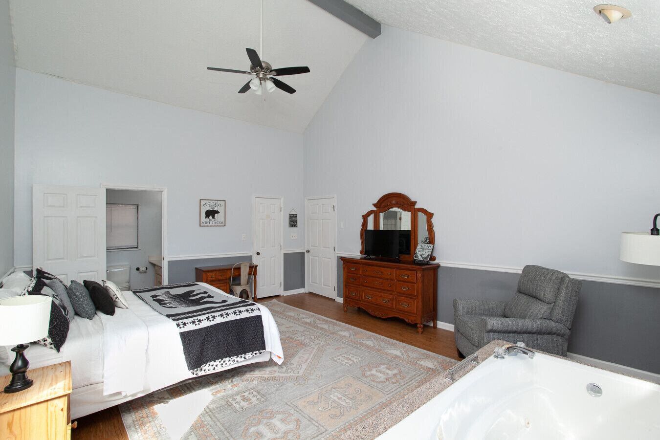Une chambre à coucher comprenant un lit, une commode, une chaise, un miroir, un ventilateur de plafond et une baignoire.