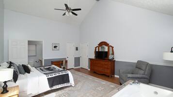 Une chambre à coucher comprenant un lit, une commode, une chaise, un miroir, un ventilateur de plafond et une baignoire.